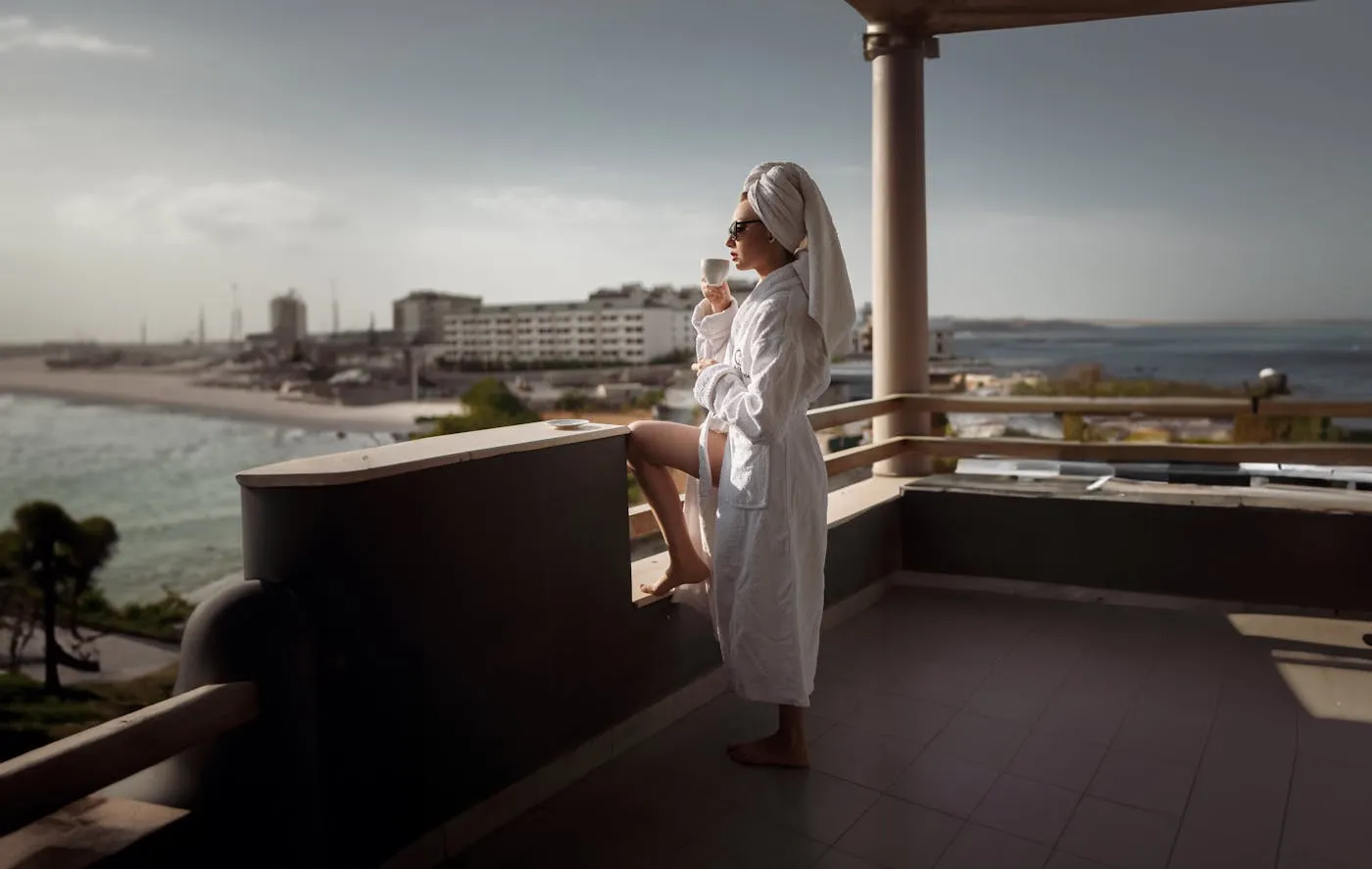A guest in a robe enjoying a coffee on a sunny balcony overlooking the ocean