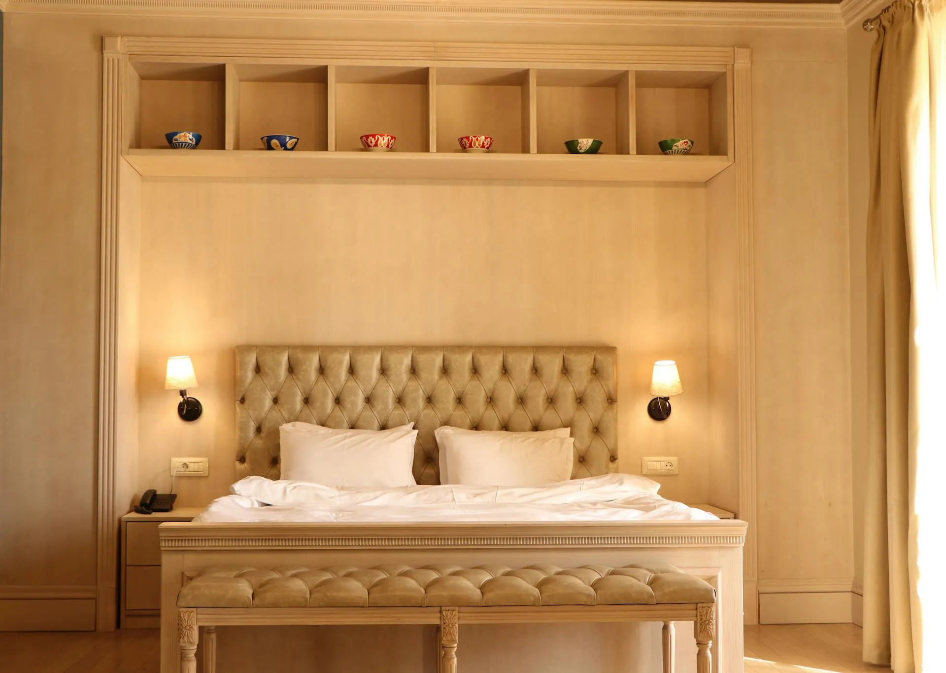 An elegant hotel suite with a tufted headboard and warm bedside lighting