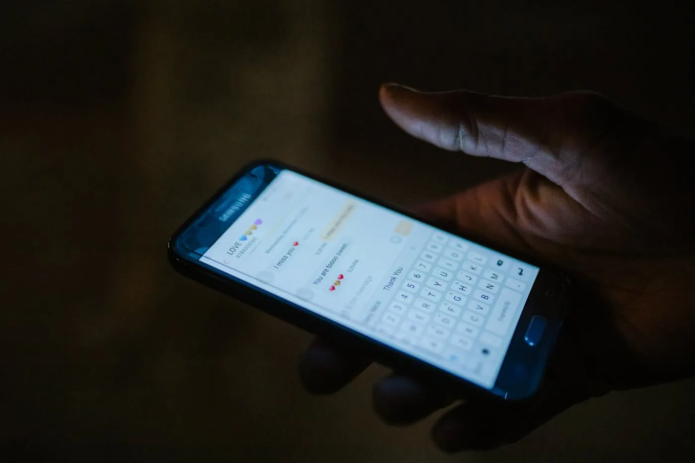 A hand holding a phone lit only by its screen in a dark room, the late-night inquiry