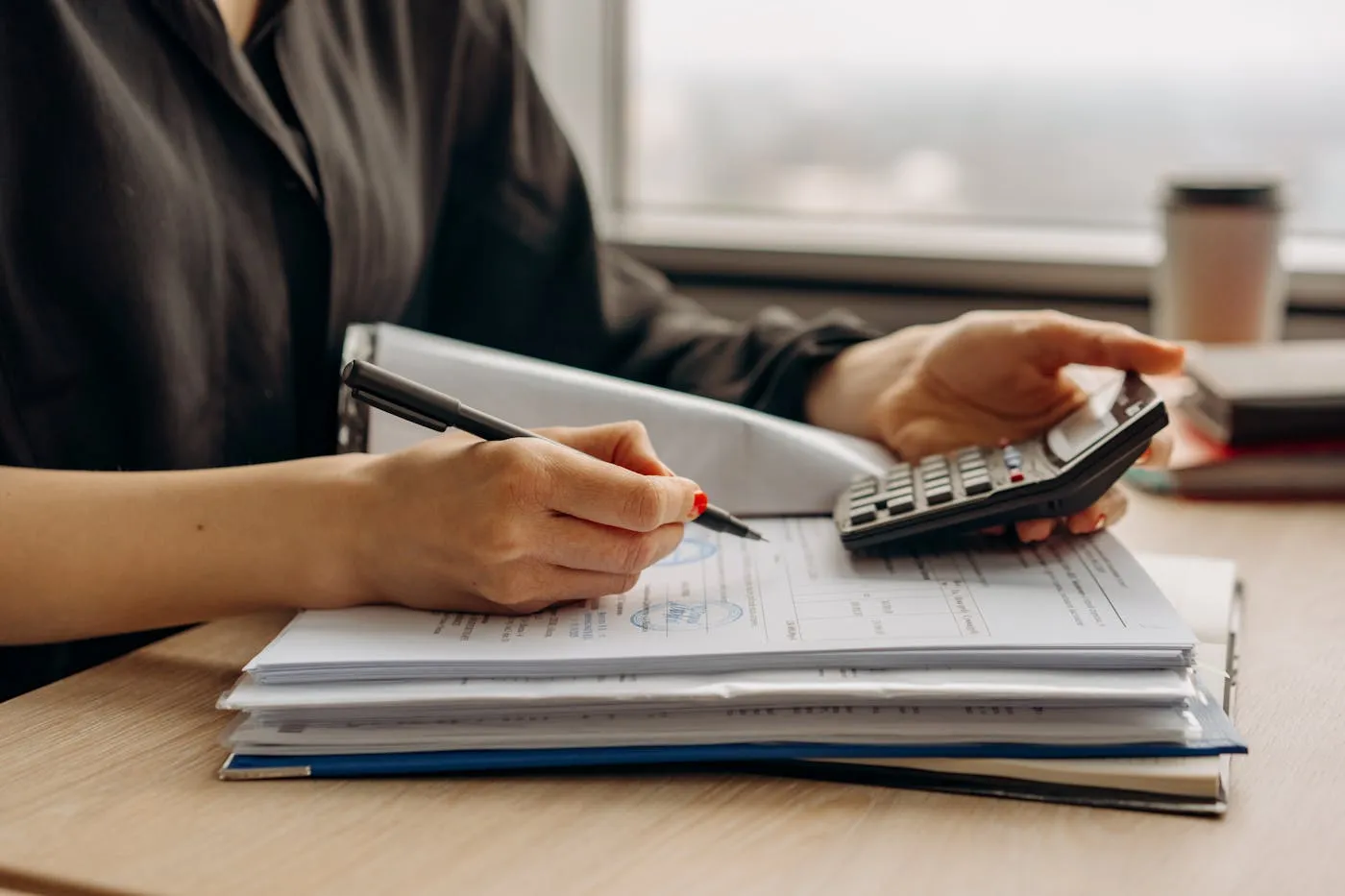 Hands checking figures on a calculator beside a printed statement and notes