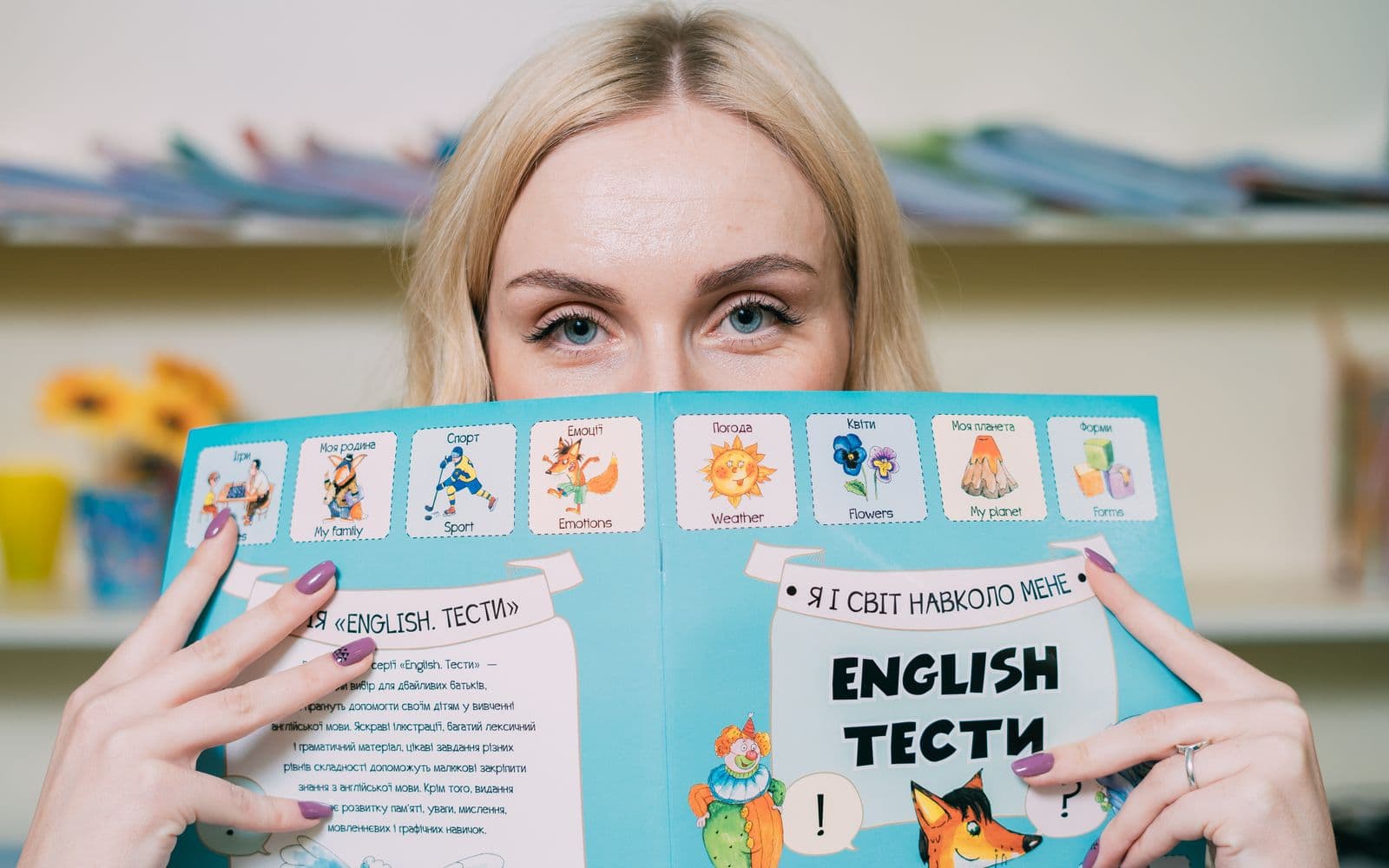 Blonde woman holding and reading an illustrated English book indoors.