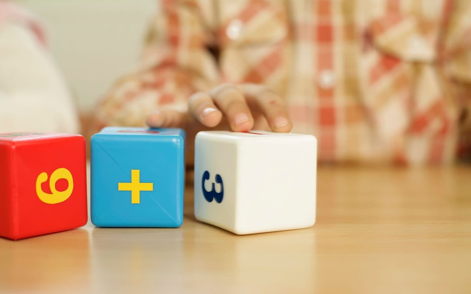 A child's hand reaching for colourful number blocks showing a 6 plus 3 sum