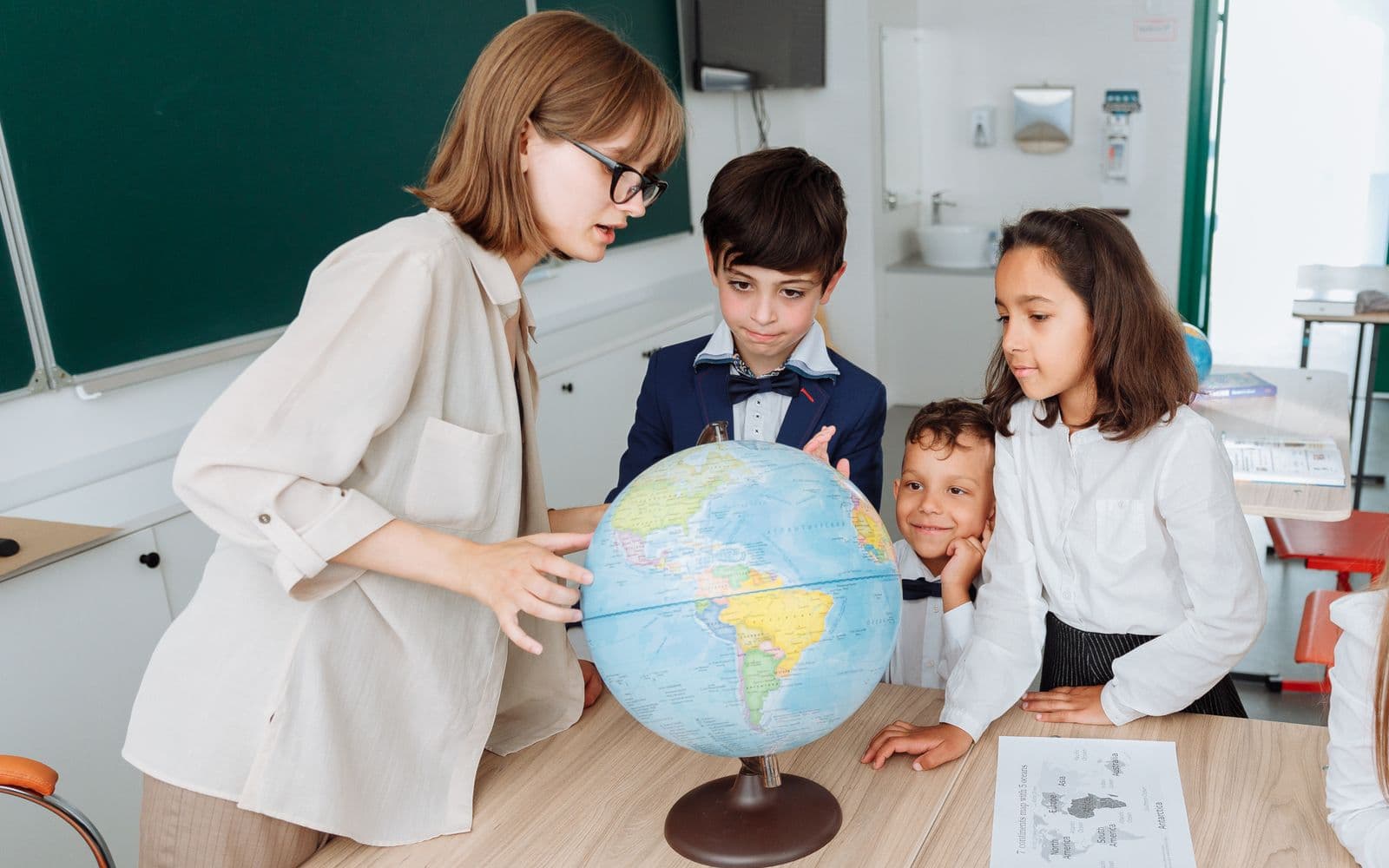 A teacher and three students examining a globe together in a classroom