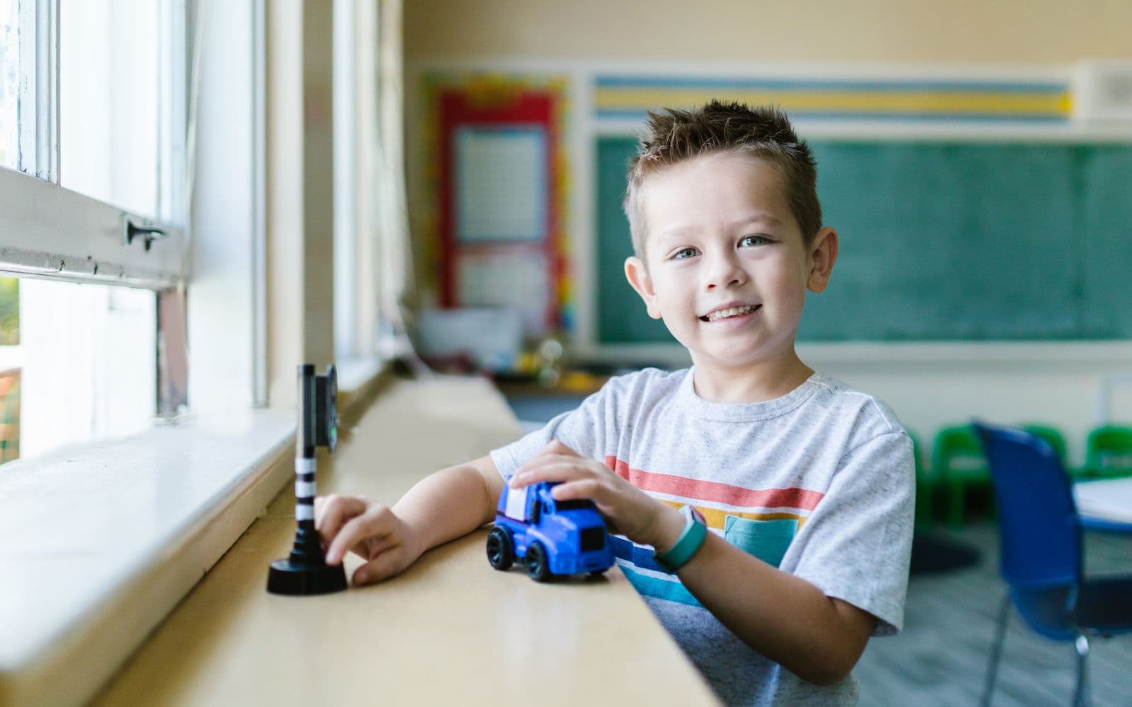 A happy child enjoys playing with a toy car in a bright classroom setting.