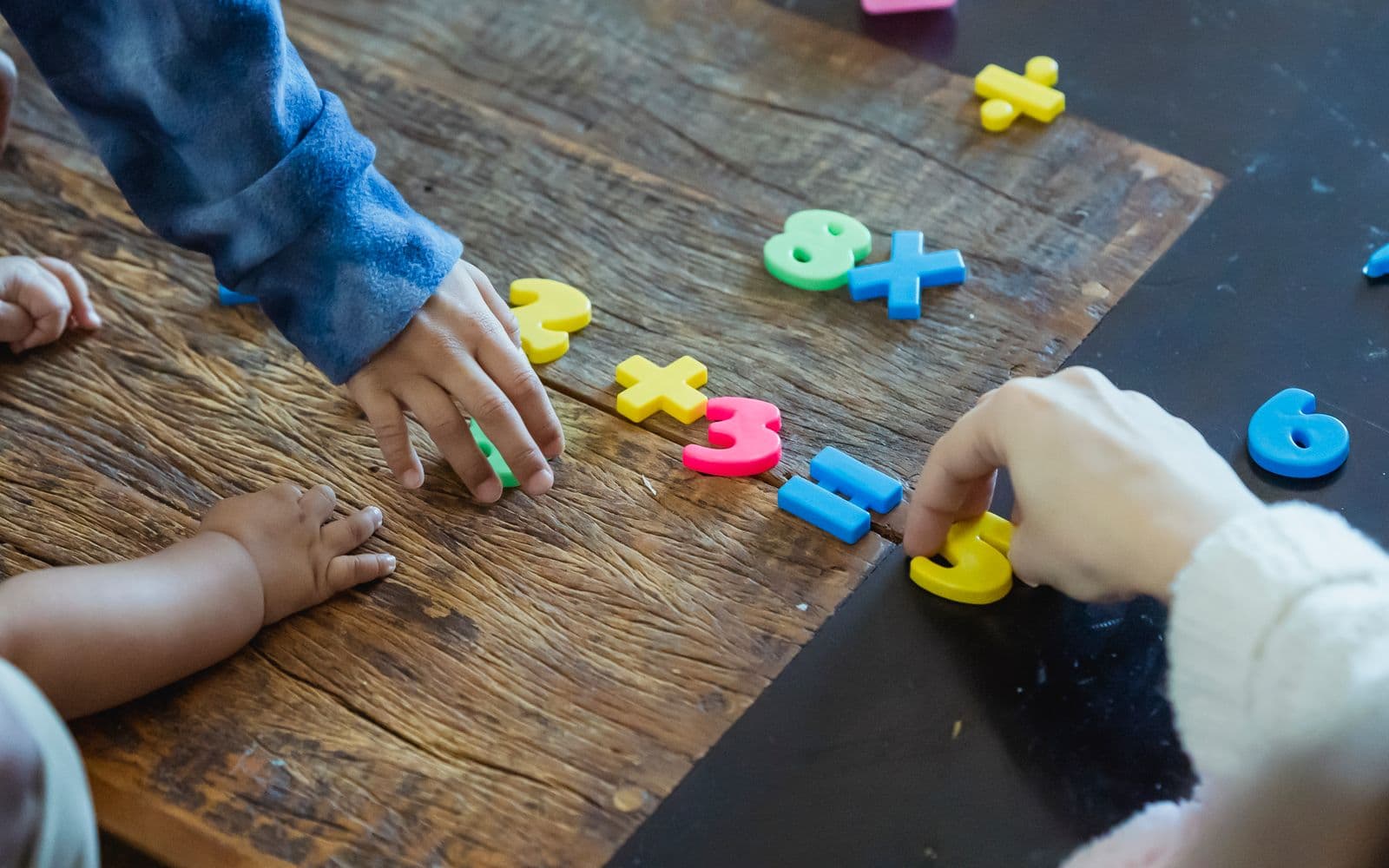 Kids engaging with colorful plastic numbers on a wooden table, fostering early math skills.