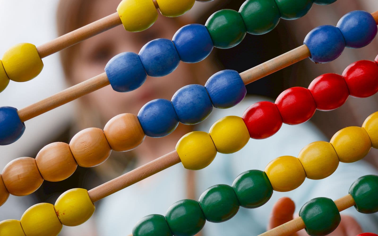 Close-up of colorful wooden abacus with a child learning math in the background, focusing on education and early childhood development.