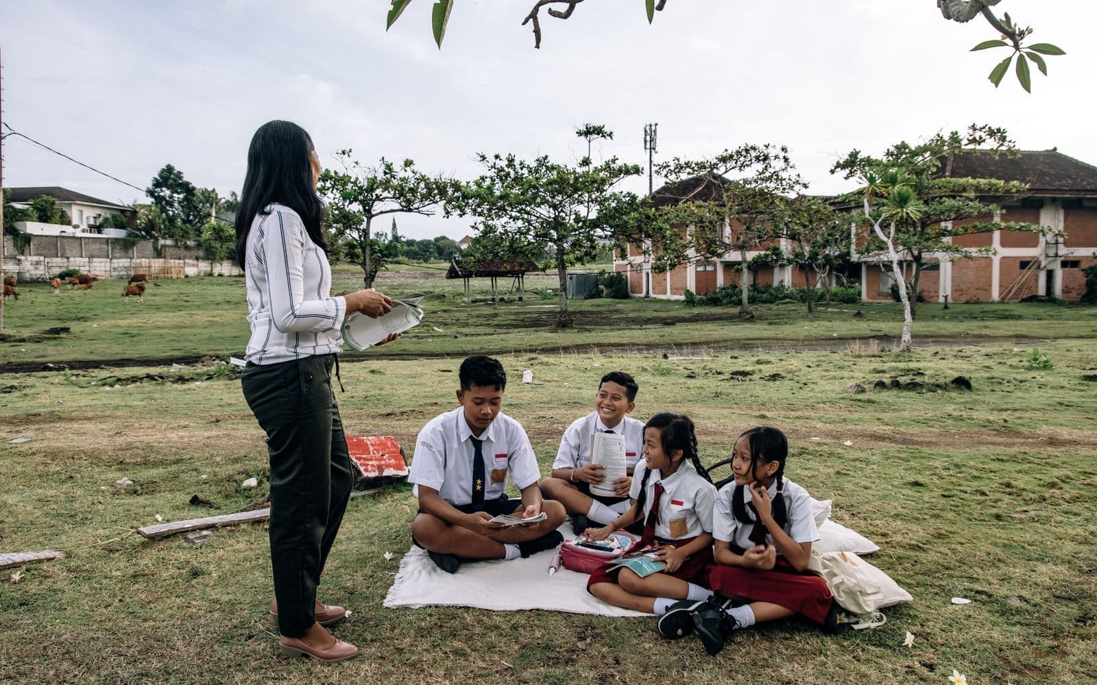 A teacher leading an outdoor lesson with four students seated on a mat in Bali